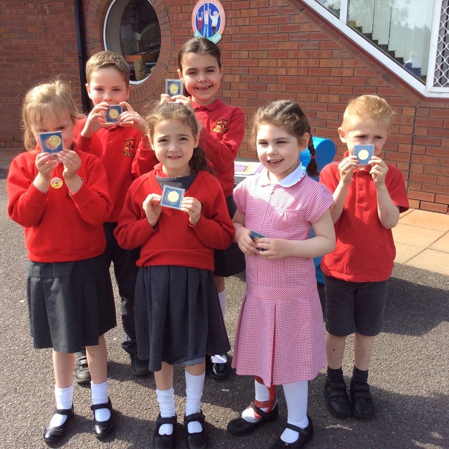 Smiling faces from pupils in P.1-P.3 display the Queen's 90th birthday coins.